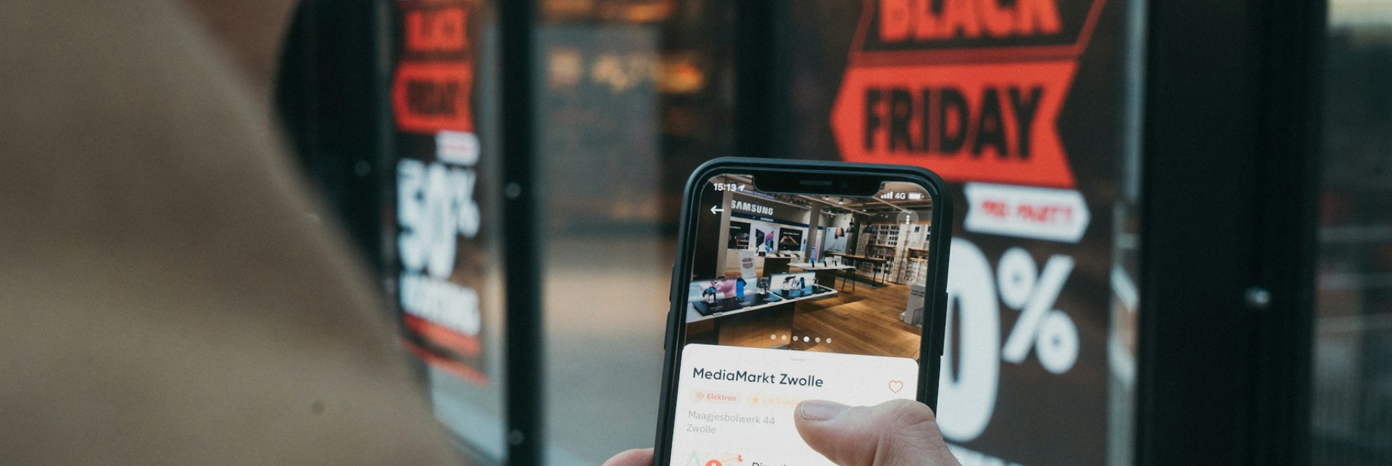 Shopper checking mobile deals with Black Friday signage