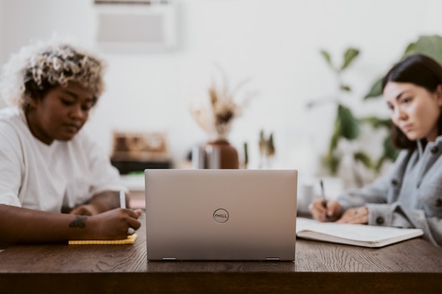 Two professionals collaborating at a wooden desk with a Dell laptop, focusing on IT security implementation