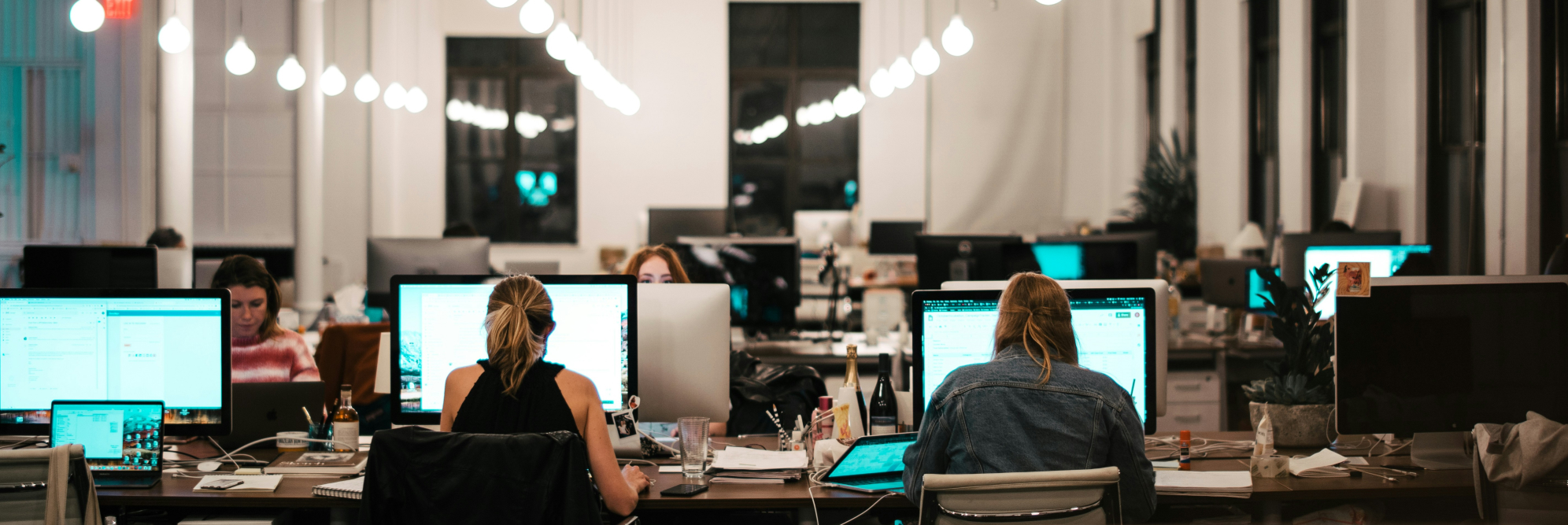 Cybersecurity team working late at monitors with modern office lighting and teal accents